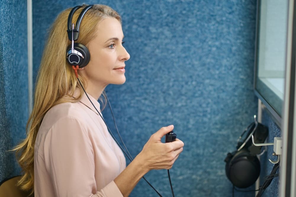 Women wearing a hearing testing headset sitting inside a sound booth
