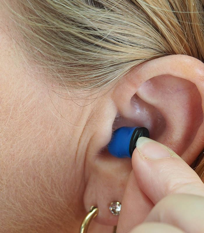 Women demonstrating how to wear an earplug for hearing protection