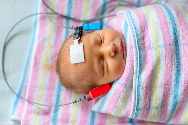 A newborn with closed eyes during a hearing screening at Denton Hearing Health Care